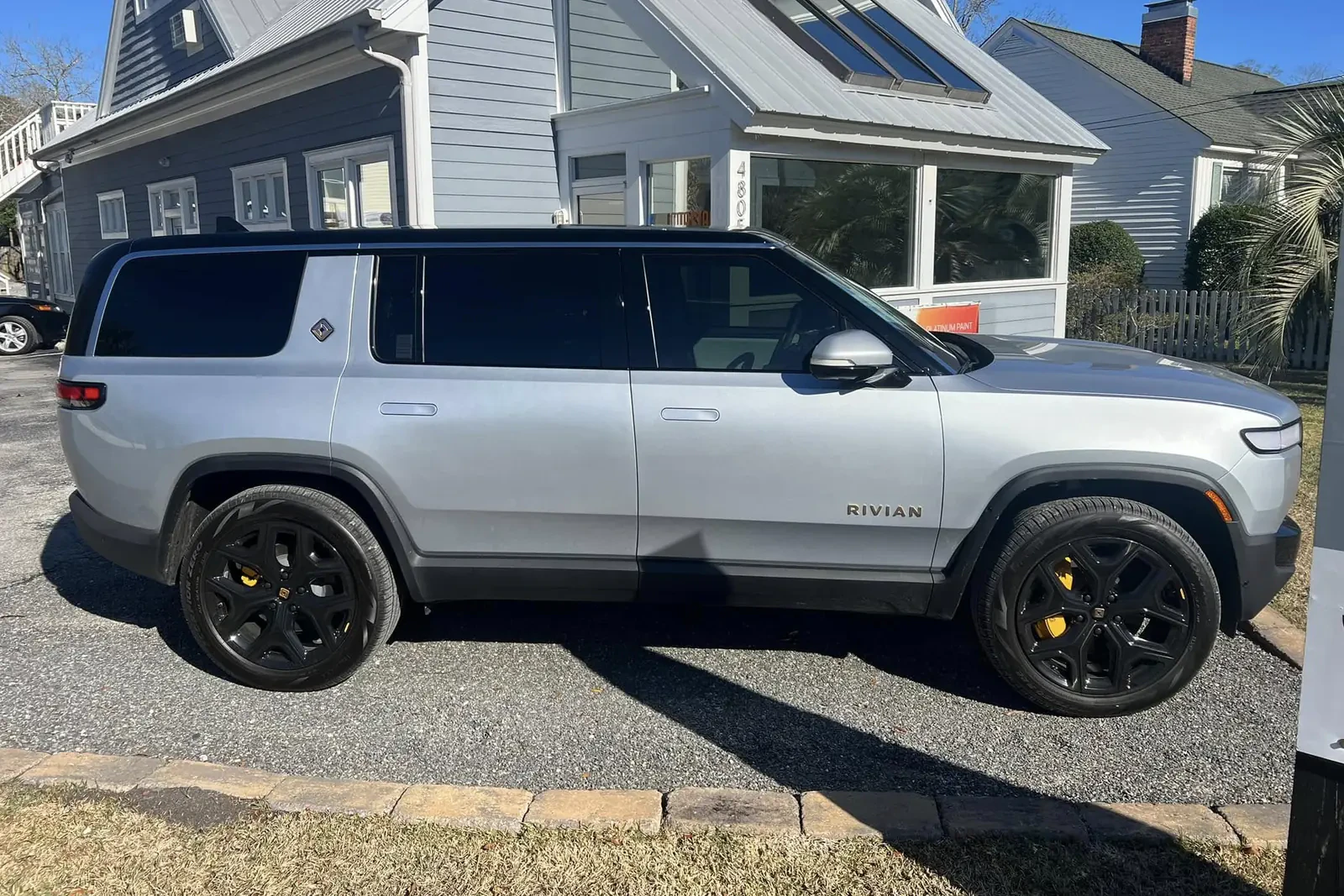 Side view of a silver Rivian SUV with tinted windows outside Coastal Glass Tinting