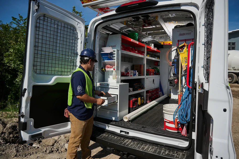 Commercial work van interior with installed shelving, drawers, ladder storage, and organized equipment