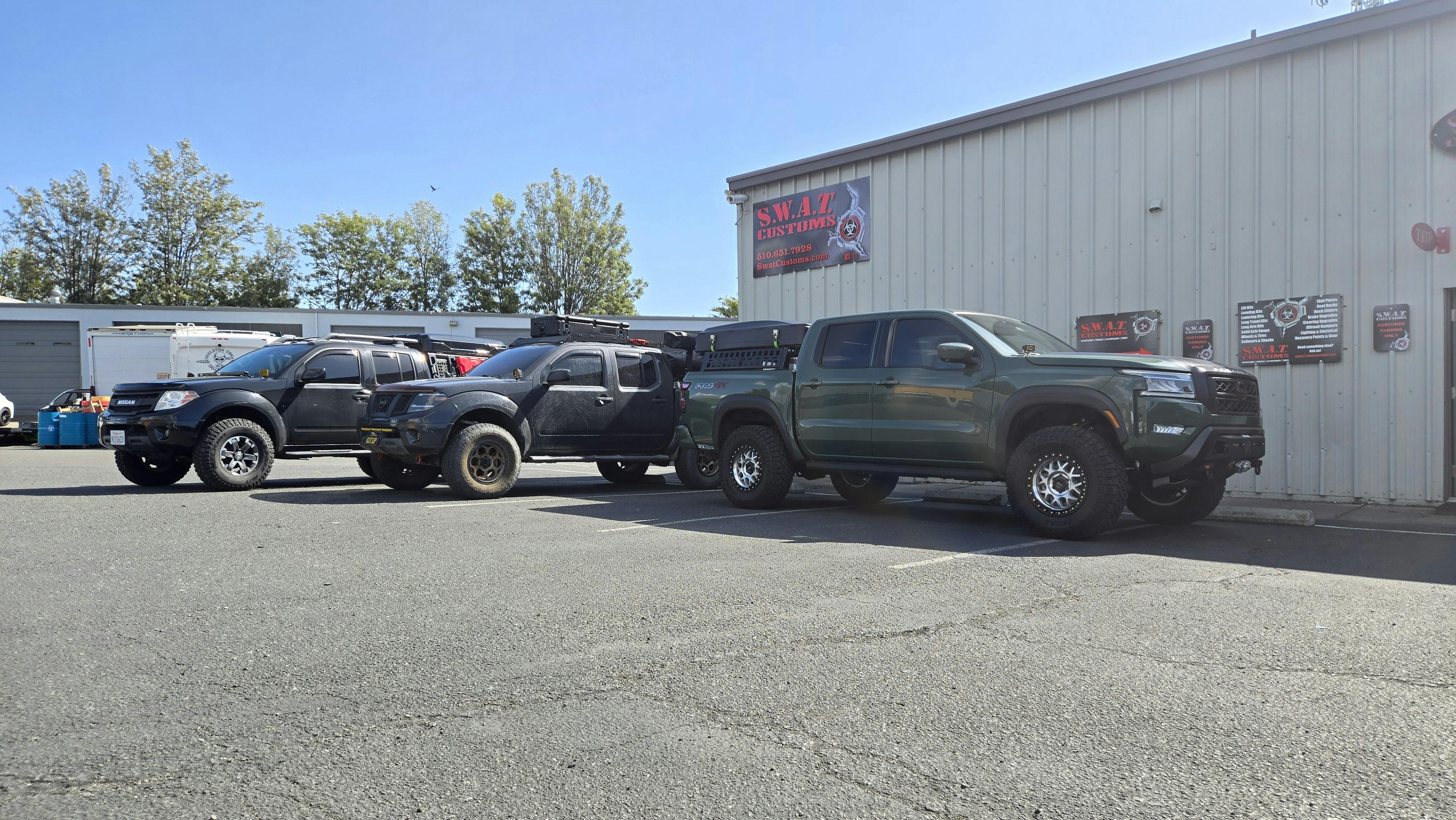 3 Lifted Nissan Frontiers Parked in front of SWAT Customs