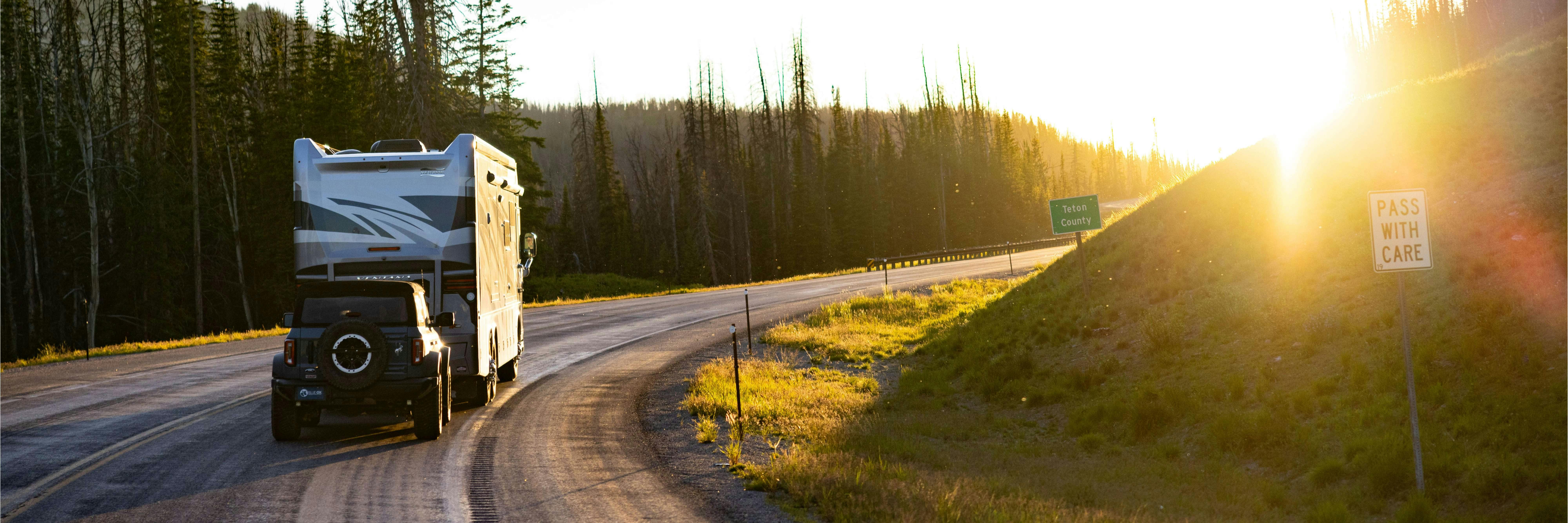 Truck towing an RV on a scenic highway at sunset — flat tow services by Trademasters.